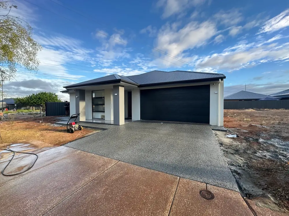 Completed concrete driveway leading to a modern suburban home with a dark garage door