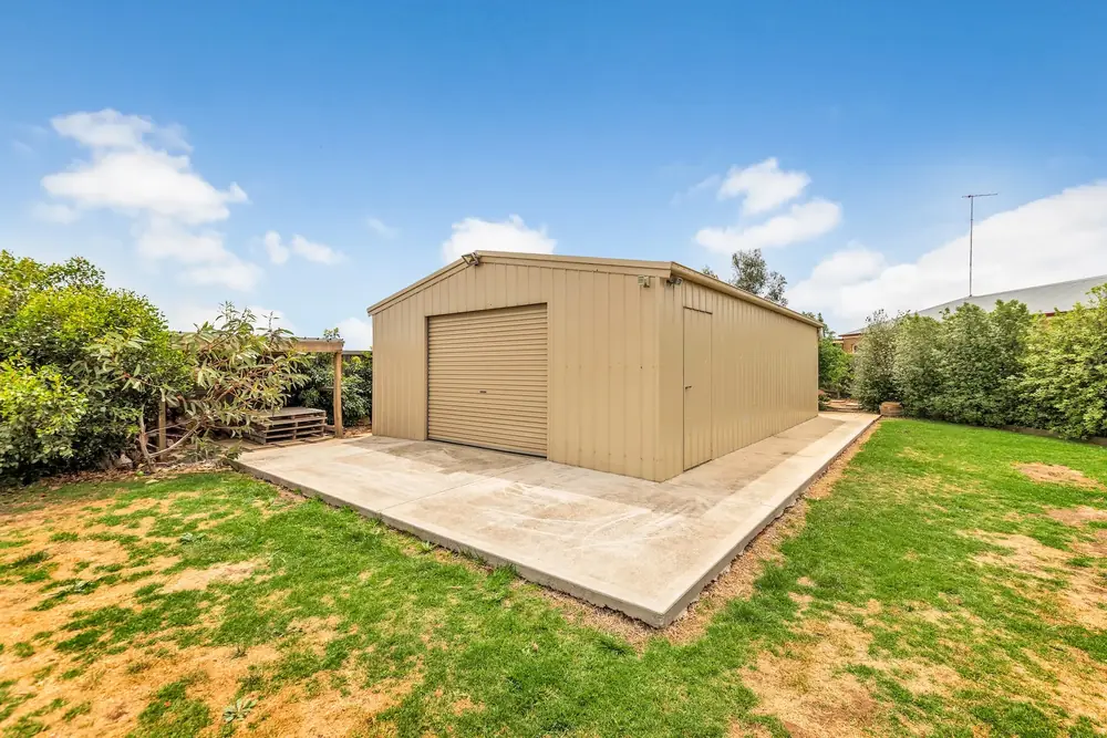 Concrete apron in front of a beige metal shed surrounded by lawn and trees